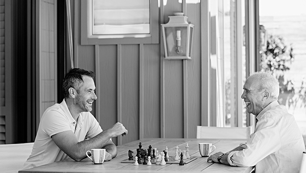 adult son and father playing chess