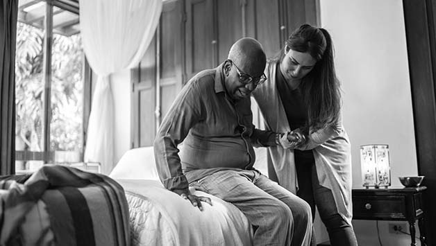 aide helping senior man stand up from bed