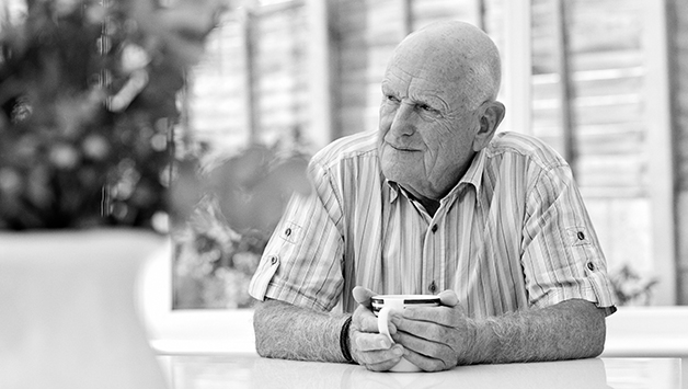 older man holding cup of coffee at table