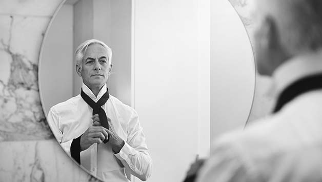 man tying tie in mirror